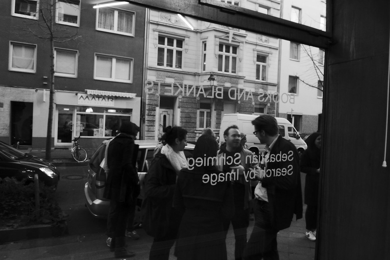 Digital-Soirée 1 — the lit window from the street, the crowd inside